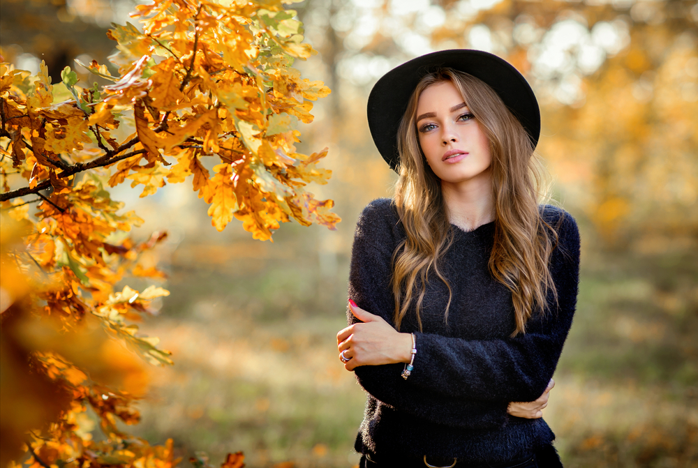 portrait of a girl in dark dress and black hat standing near colorful autumn leaves