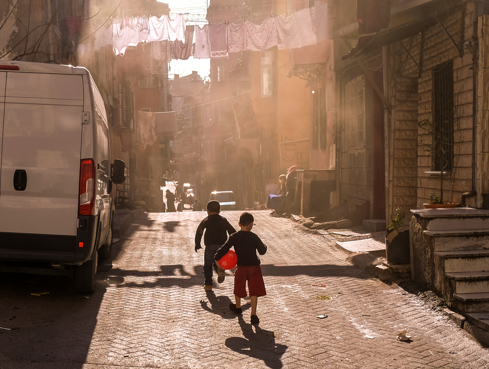 Two boys play with a red ball in the street